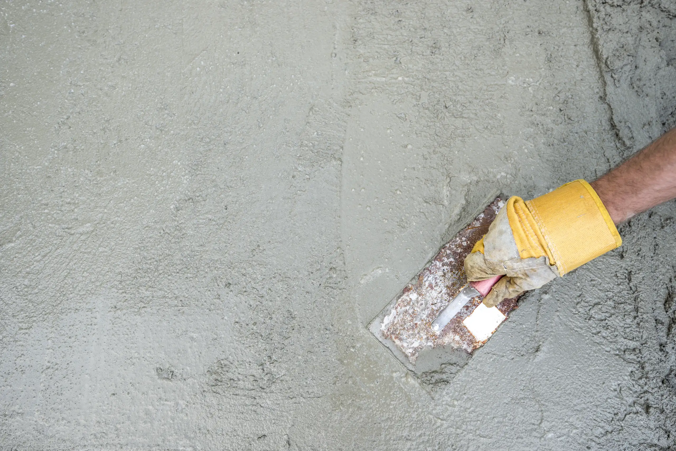 Hand eines Arbeiters mit Kelle, die frischen Beton für Pflasterarbeiten glättet