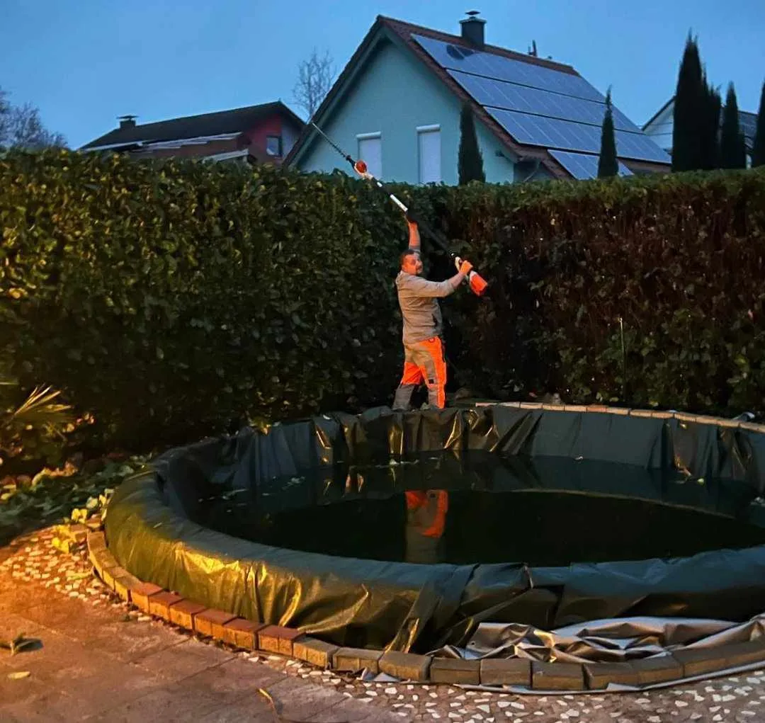 Mitarbeiter schneidet eine Hecke über einem Poolrand mit einem elektrischen Heckenschneider
