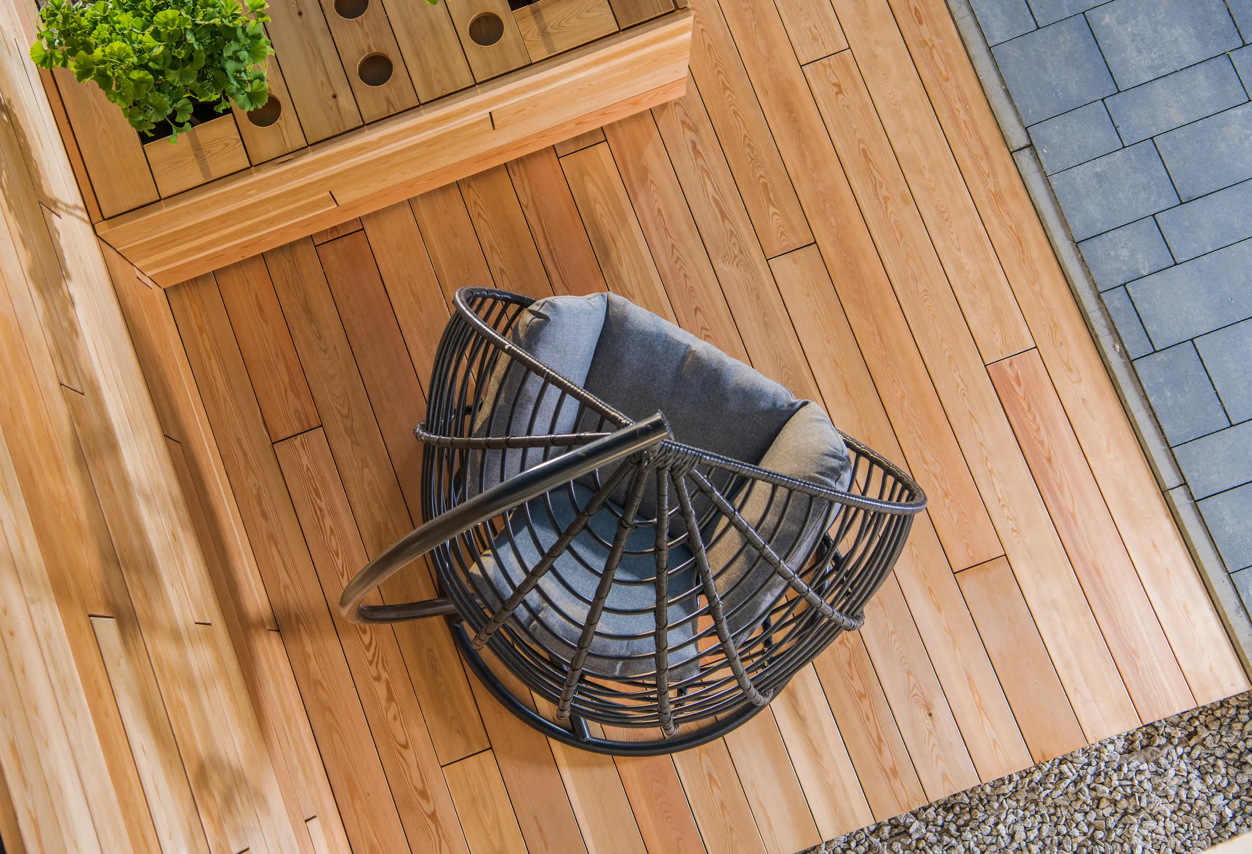 Moderne Holzterrasse mit stylischem hängendem Stuhl und gepflegten Bepflanzungen