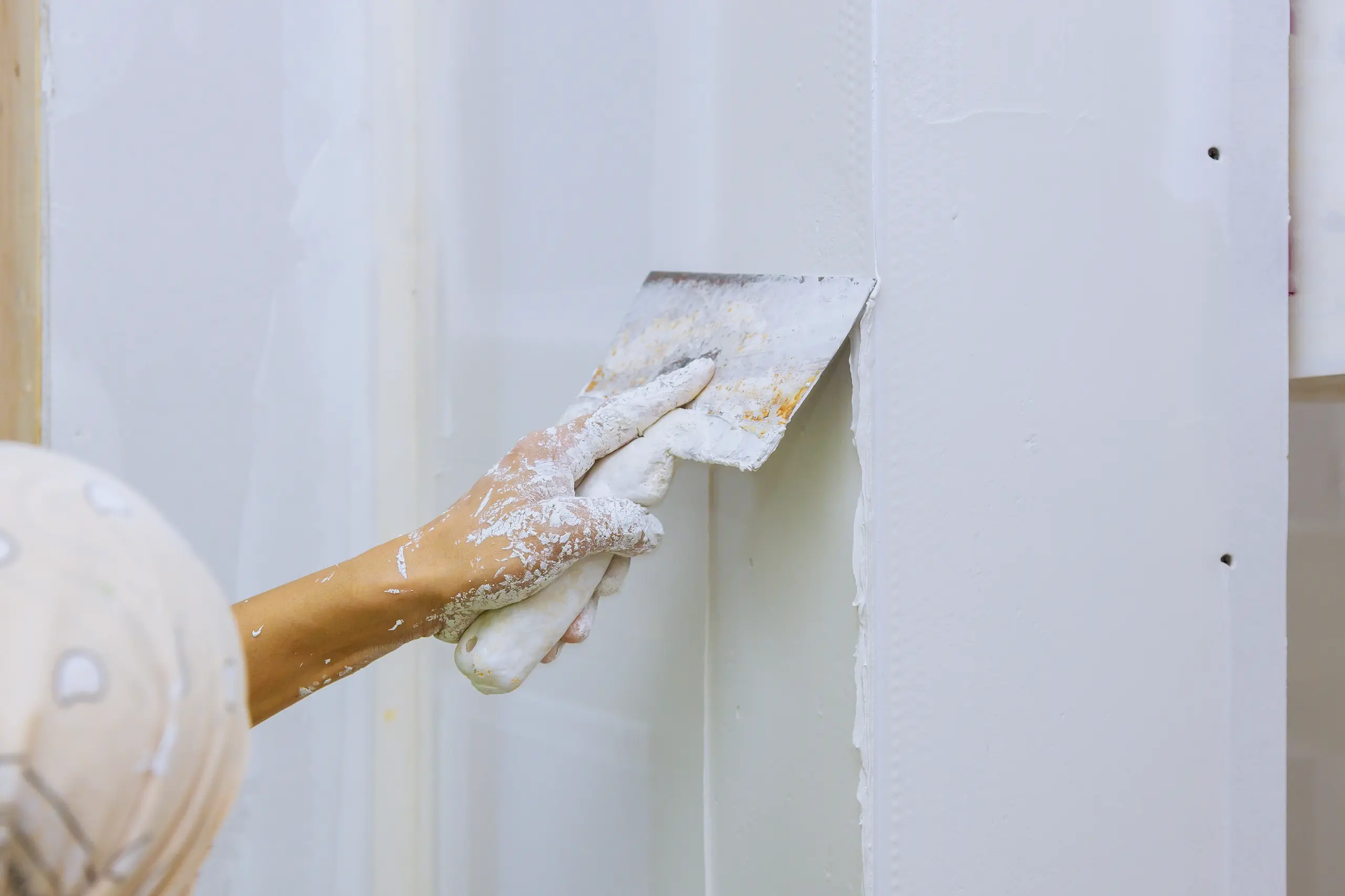 Hand, die einen Spachtel mit frischer Spachtelmasse an einer Wand führt
